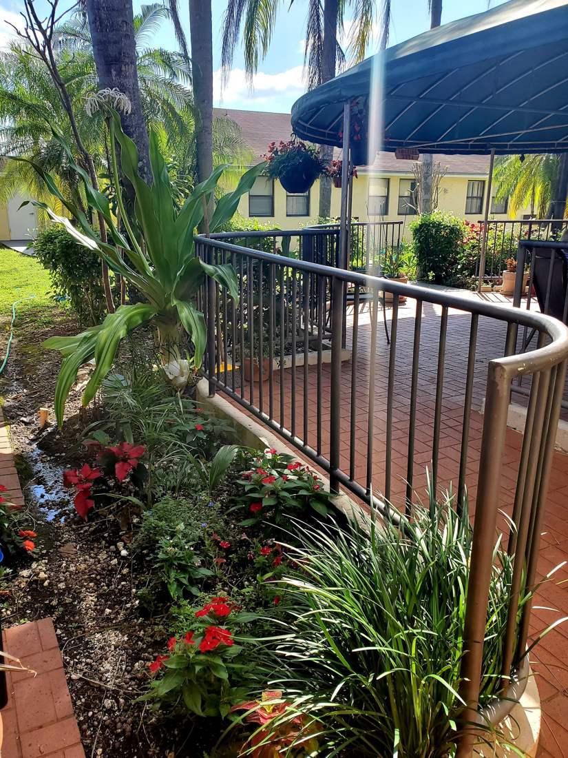 Covered patio with a railing and planted flower beds at Sunny Hills in Homestead